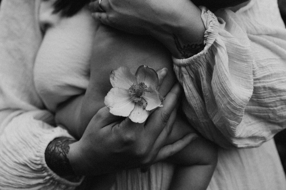 black and white photo of a newborn in his mother's arms with a flower