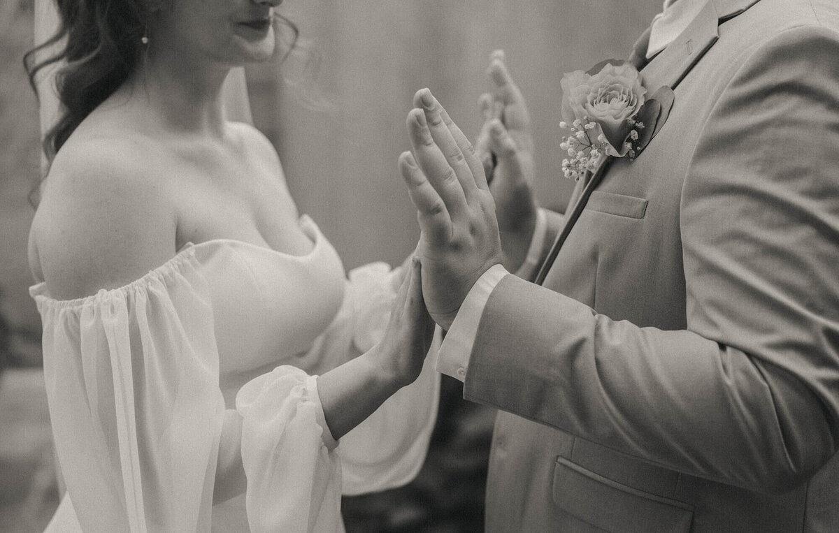 Close up of a bride and groom with the palms of their hands placed against each other during their first looks.