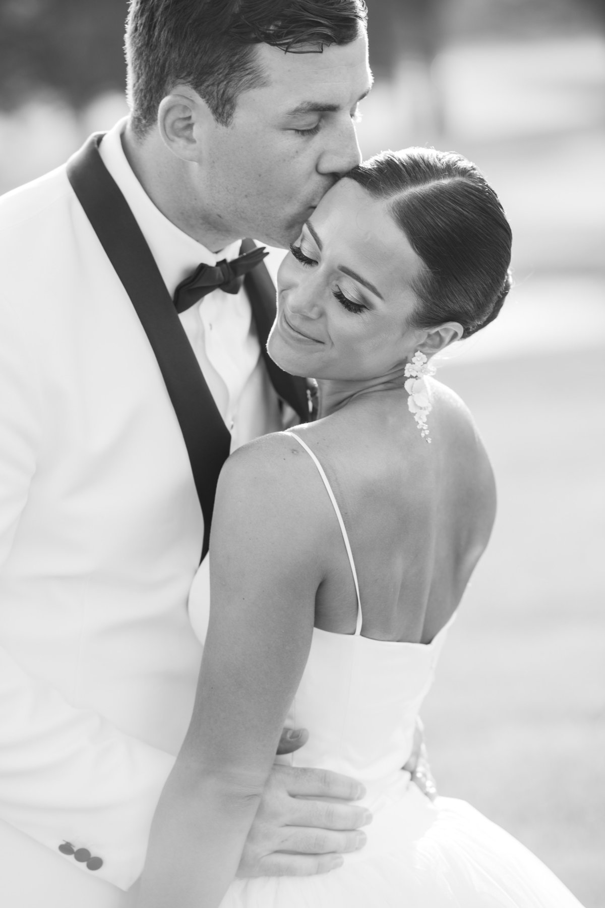 groom kissing bride on forehead in black and white photo from wedding at The Muttontown Club