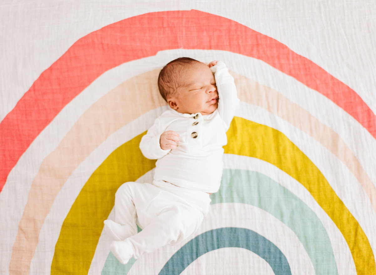 Baby laying on a rainbow blanket and stretching during a Raleigh NC newborn photo session. Photographed by newborn photographers Raleigh A.J. Dunlap Photography.
