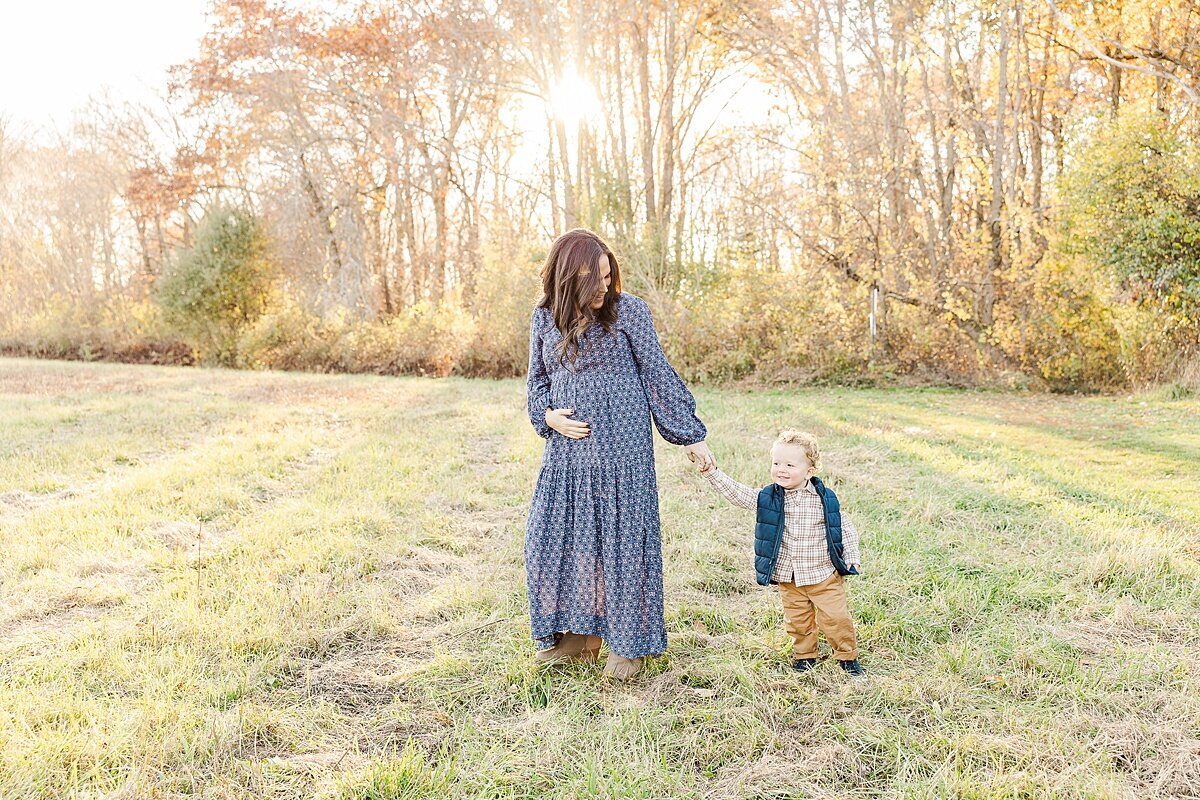 mom and son walk holding hands  during winter maternity photo session with Sara Sniderman Photography at Heard Farm in Wayland Massachusetts