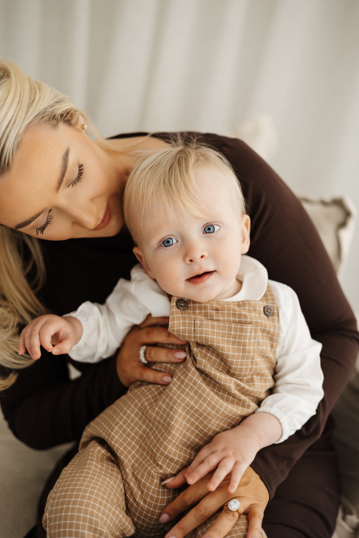 A mother holding her child and posing for the camera in browns and cream and beiges during a family studio photoshoot with lucy jane photography in christchurch