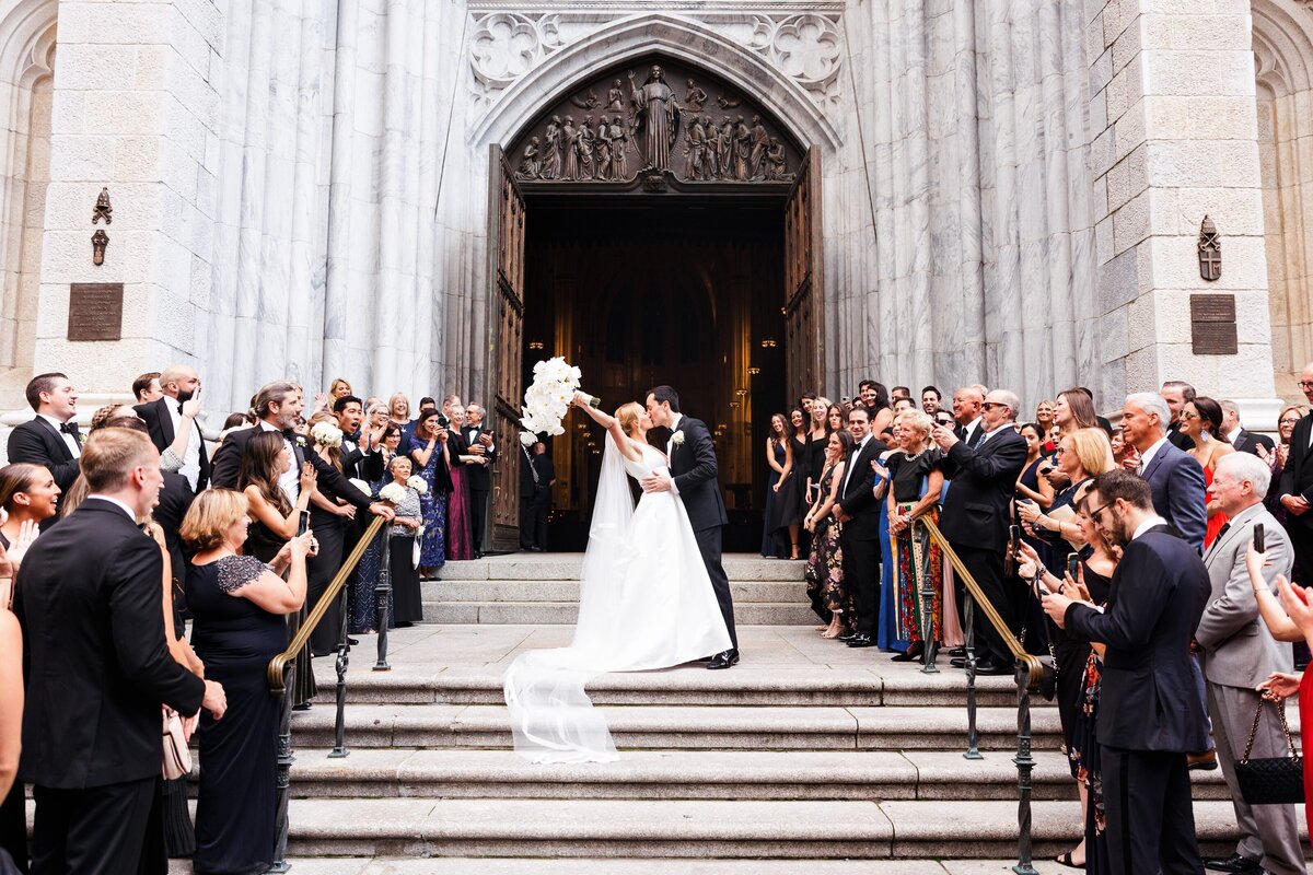 Bride and groom kissing on church steps, celebrated by guests