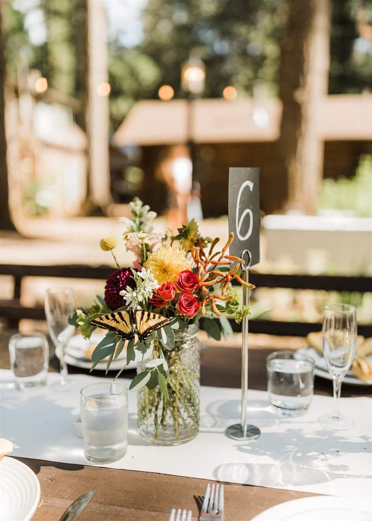 Floral arrangement sits atop a table at an outdoor summer wedding reception.