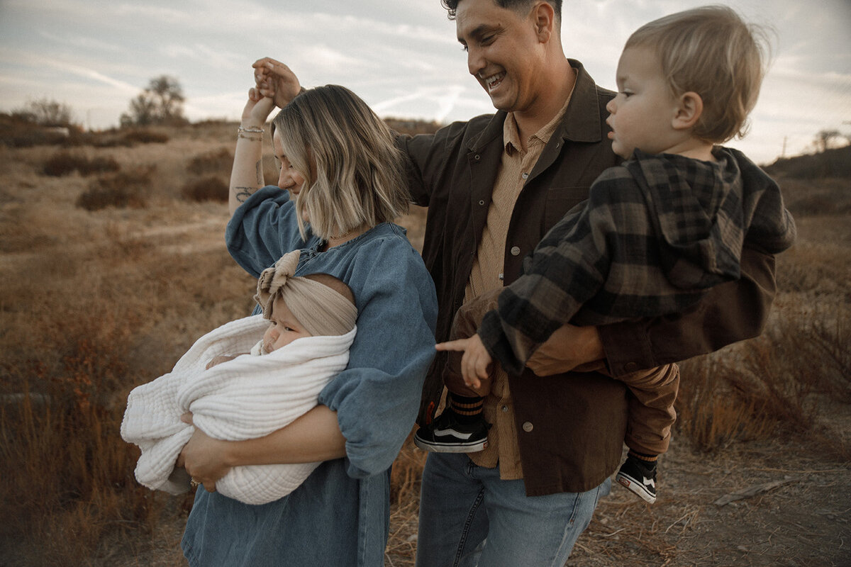 mom dad and their two children walk through field for family photos