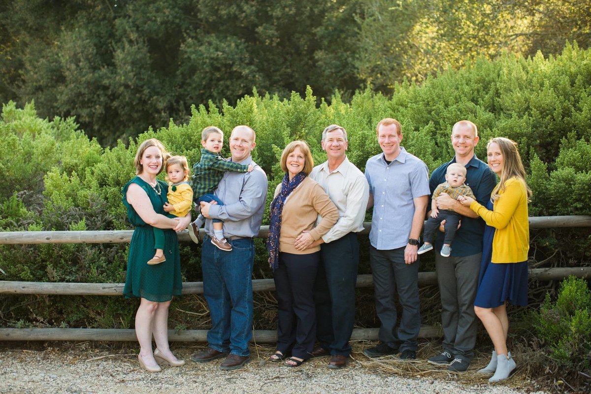 Multi-generational family pose together in a nature center with green shrubs and ranch-style fencing