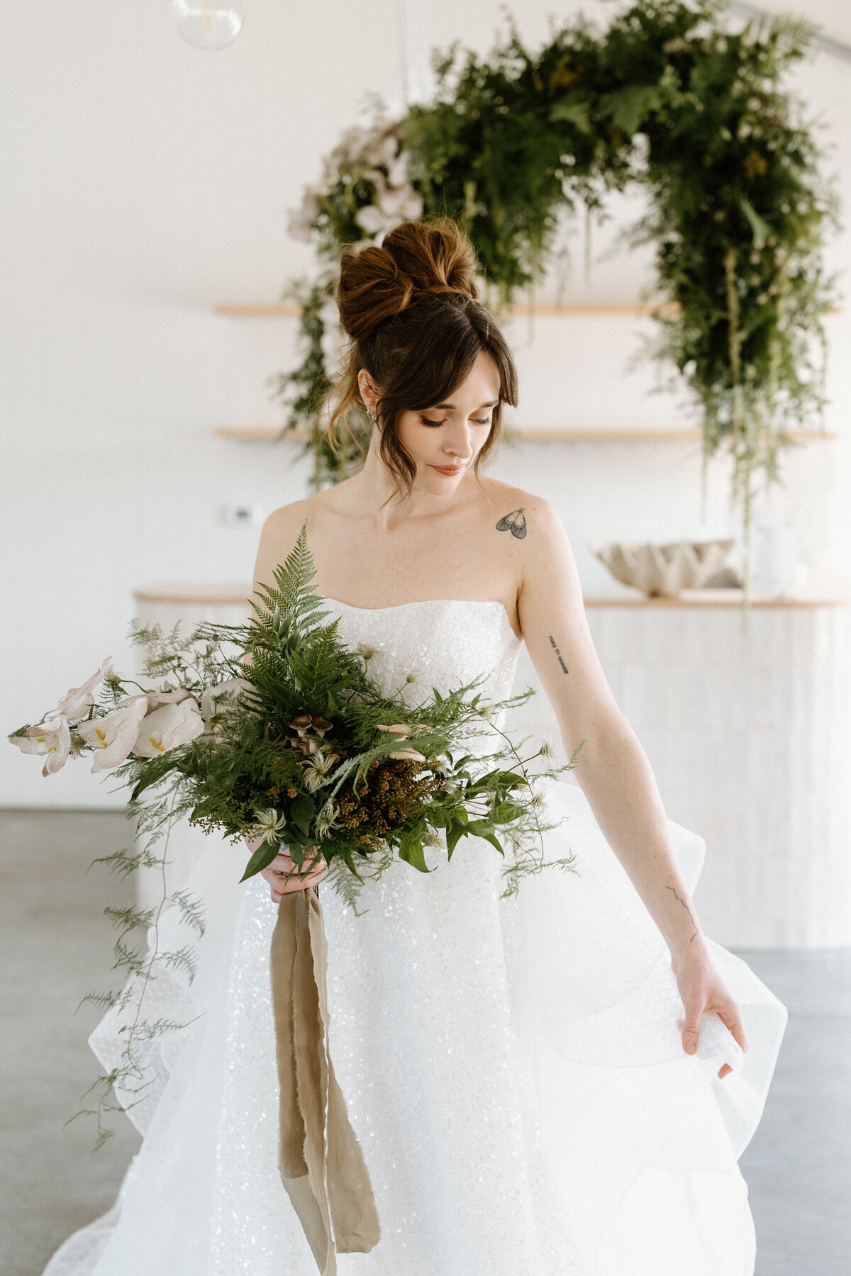 The bride admires her wedding dress while she holds her leaf bouquet