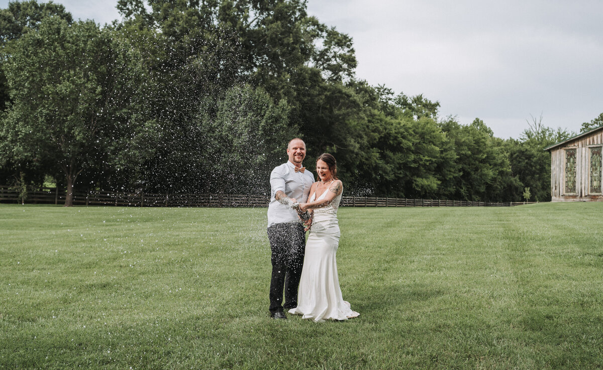 Bride and groom celebrate with a champagne pop in a wide grassy field at The Gentry Farm in Danville, Virginia.