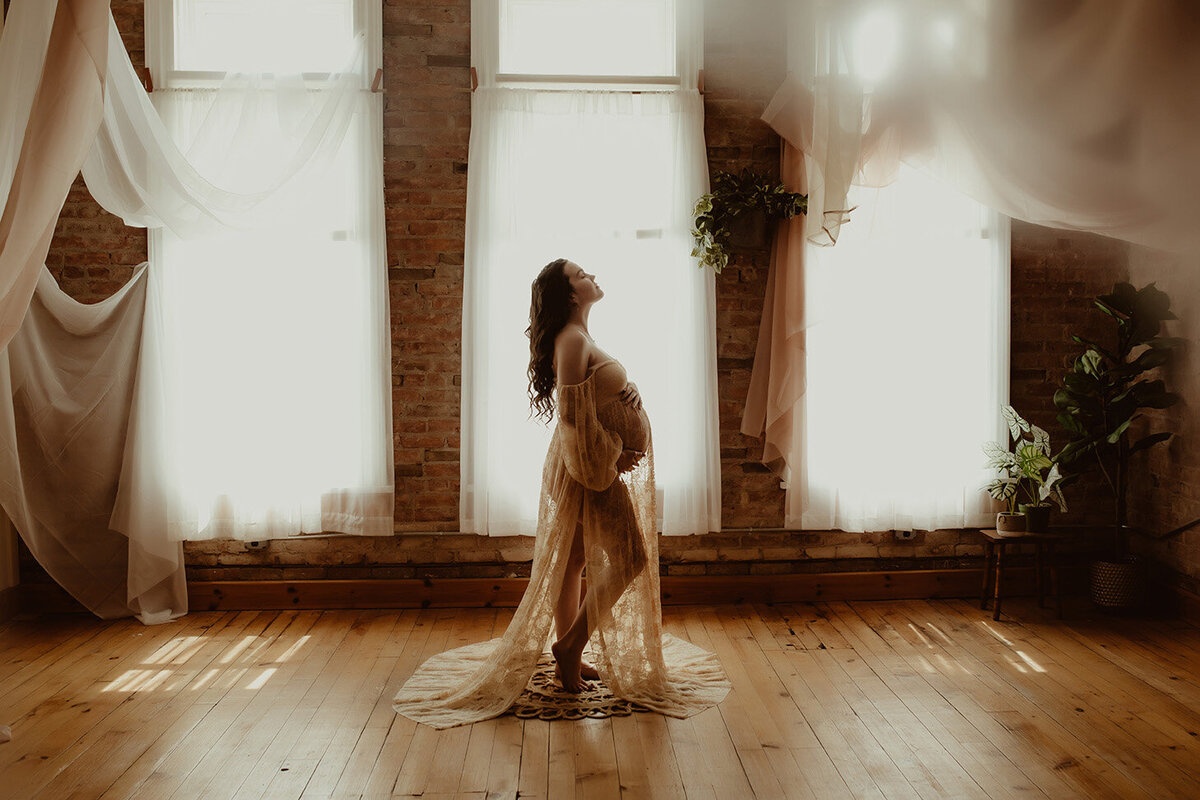 a pregnant woman standing in a beautiful natural light studio