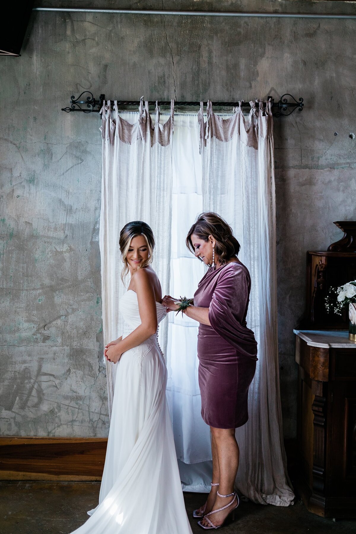 Mother of the bride helping her daughter into her wedding dress for her wedding day at Olde Dobbin Station.