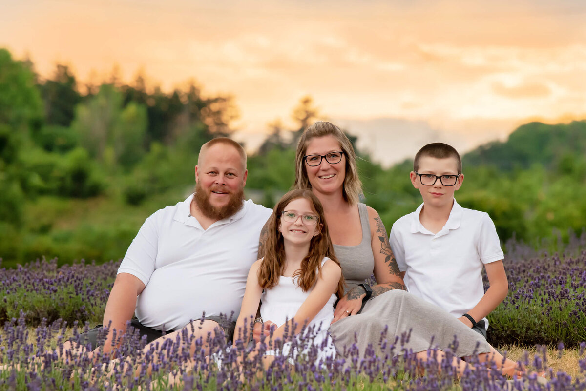 Mom and dad with their teenage son and daughter sitting on the ground in the lavender with the golden sunset behind them for their Burlington, Ontario family photographer session