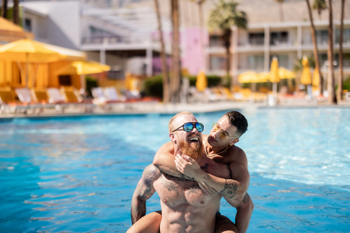 High-energy poolside moment between two models laughing and splashing, set against a colorful Palm Springs backdrop.