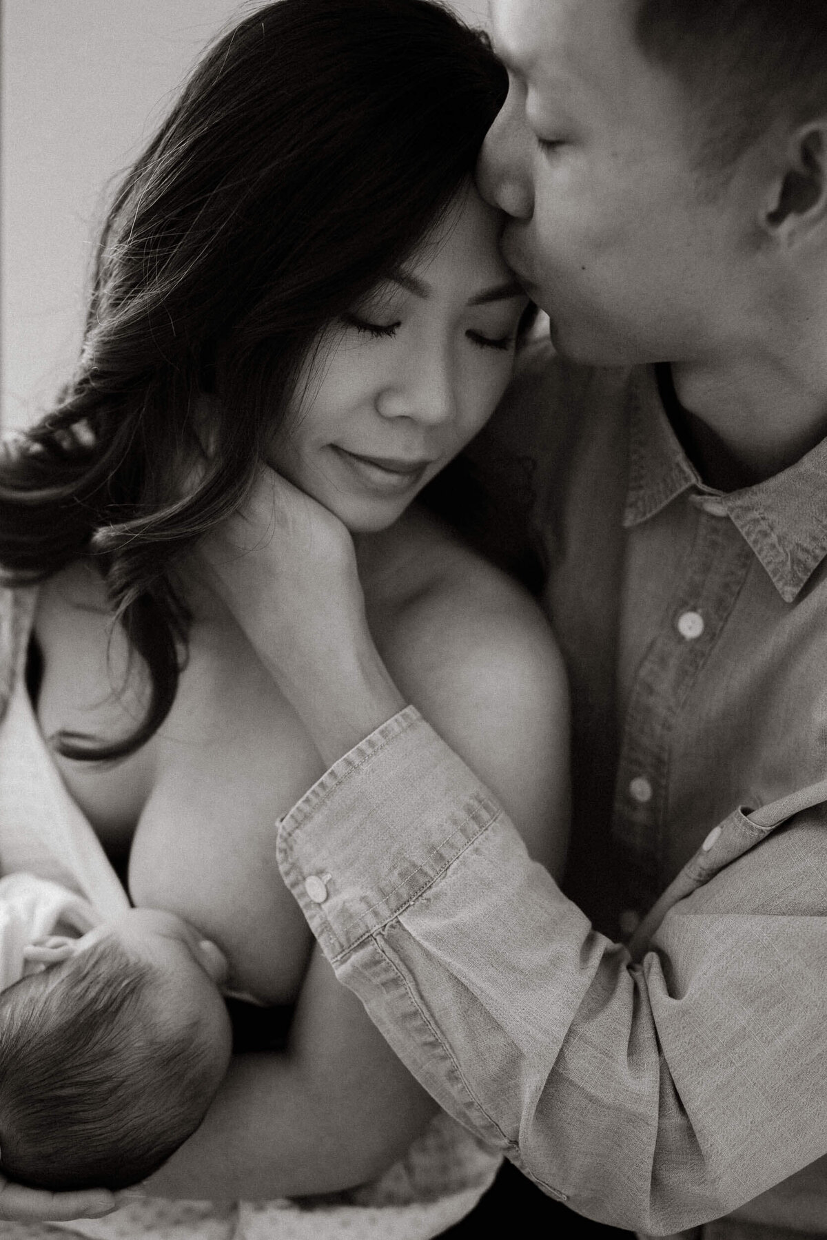 Black and white lifestyle newborn family photo of mother breastfeeding surrounded by love.