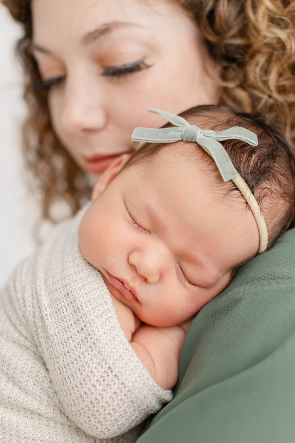 Newborn baby sleeping on mom's shoulder. Mom's face is blurred out in the background.