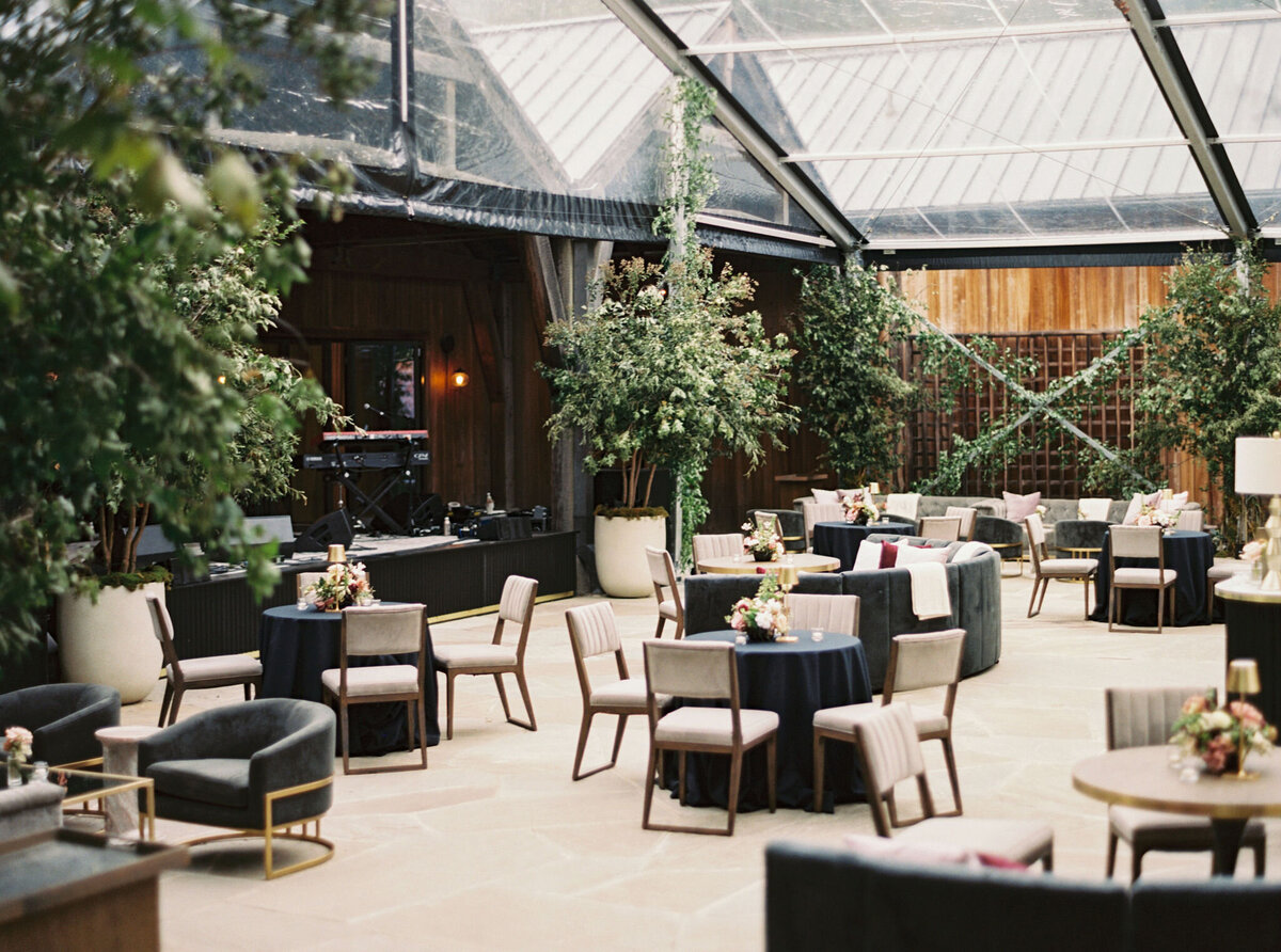 Moody welcome party for fall wedding weekend. Tented reception for outdoor wedding reception at Blackberry Farm. Moody floral design with colors of deep magenta, mauve, eggplant, blush, and natural greens. Rich tones with roses, mums, and smokebush foliage. Romantic candle light and large trees create a magical setting for a welcome party. Destination wedding at Blackberry Farm. Design by Rosemary & Finch Floral Design in Nashville, TN.