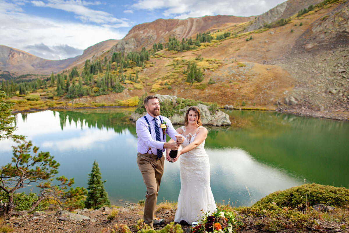 Newlyweds pop a bottle of champagne after their elopement ceremony at an alpine lake