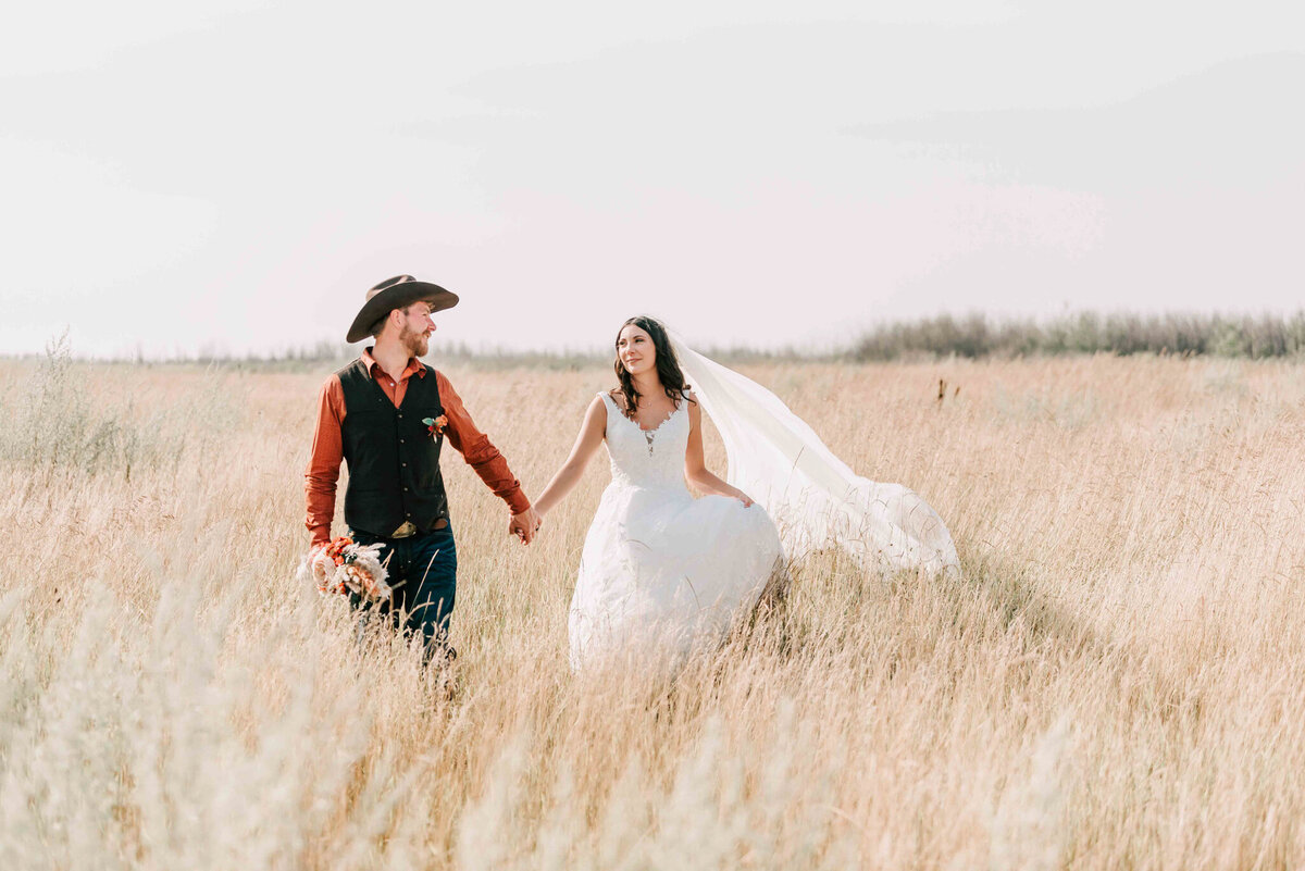 Bride and groom walk towards the camera holding hands and looking at each other. 