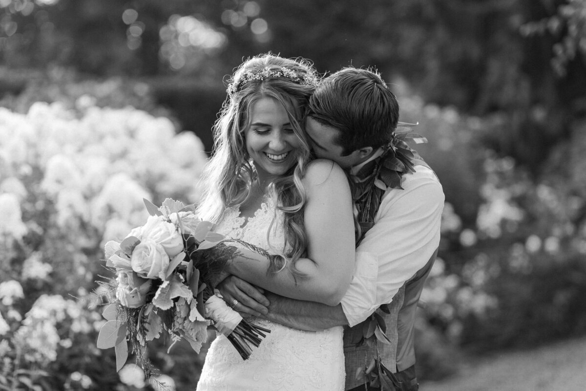 Bride-and-groom-snuggle-and-kiss-in-a-big-field-of-flowers-at-wedding-venue-Twin-Willow-Gardens-in-Snohomish-WA-photo-by-Joanna-Monger-Photography