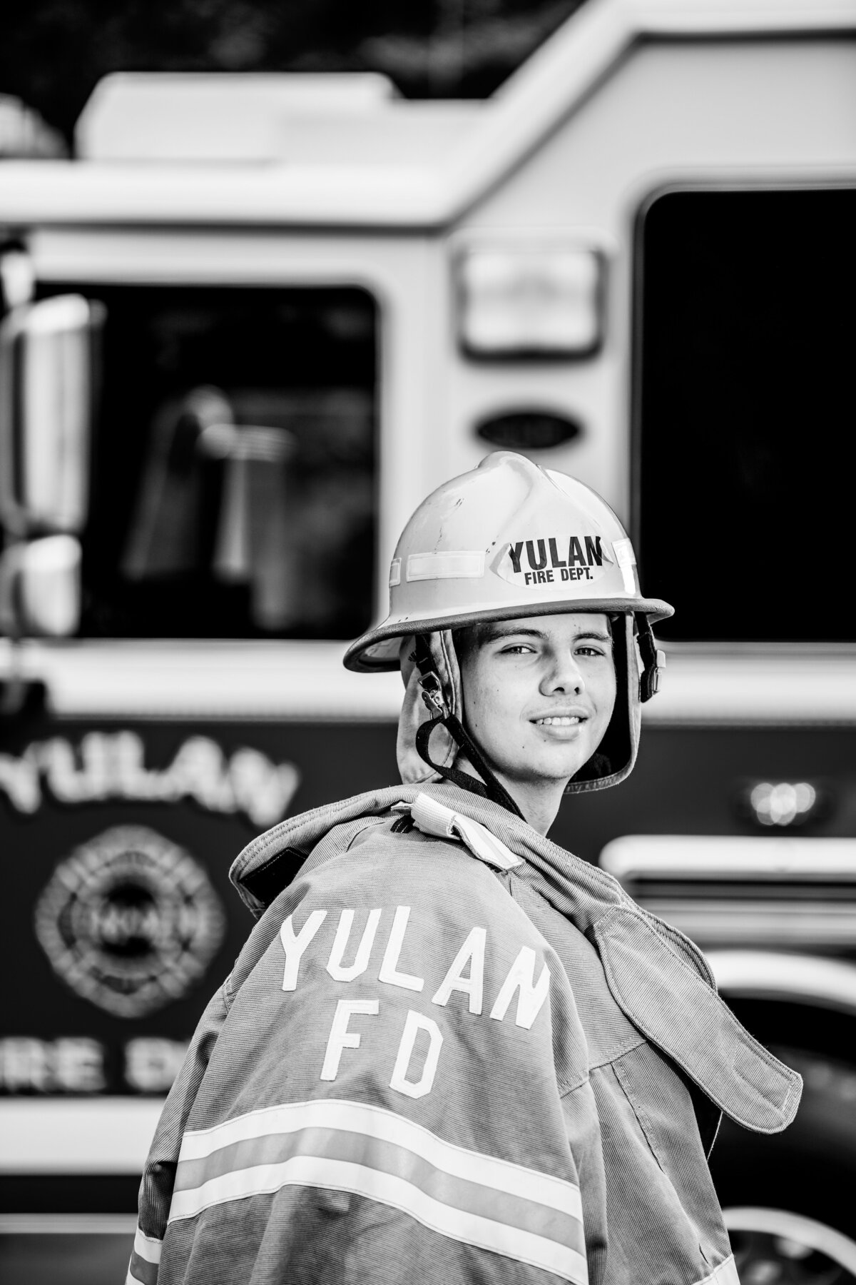 a yulan new york firefighter wears his turnout gear while standing in front of a yulan firetruck