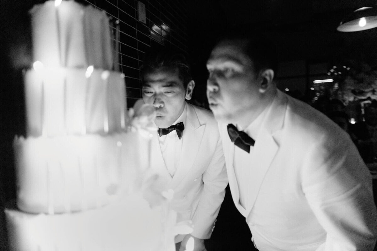 The two grooms are blowing the candles on their wedding cake in The Skylark, New York. Wedding Image by Jenny Fu Studio