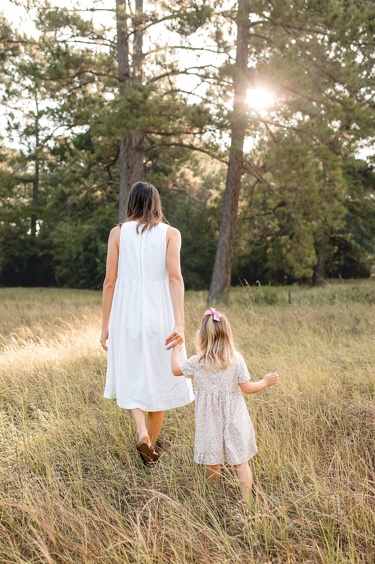 Mother leading daughter through a field by Cypress Family Photographer