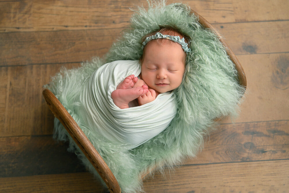 Baby girl smiling in a tiny bed for her newborn photography session.