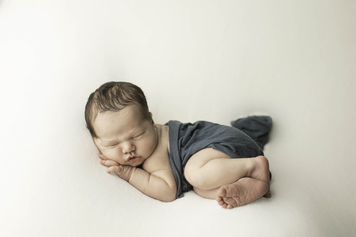 Newborn baby boy peacefully wrapped in a soft blue fabric, resting comfortably with a serene expression, creating a classic and timeless portrait