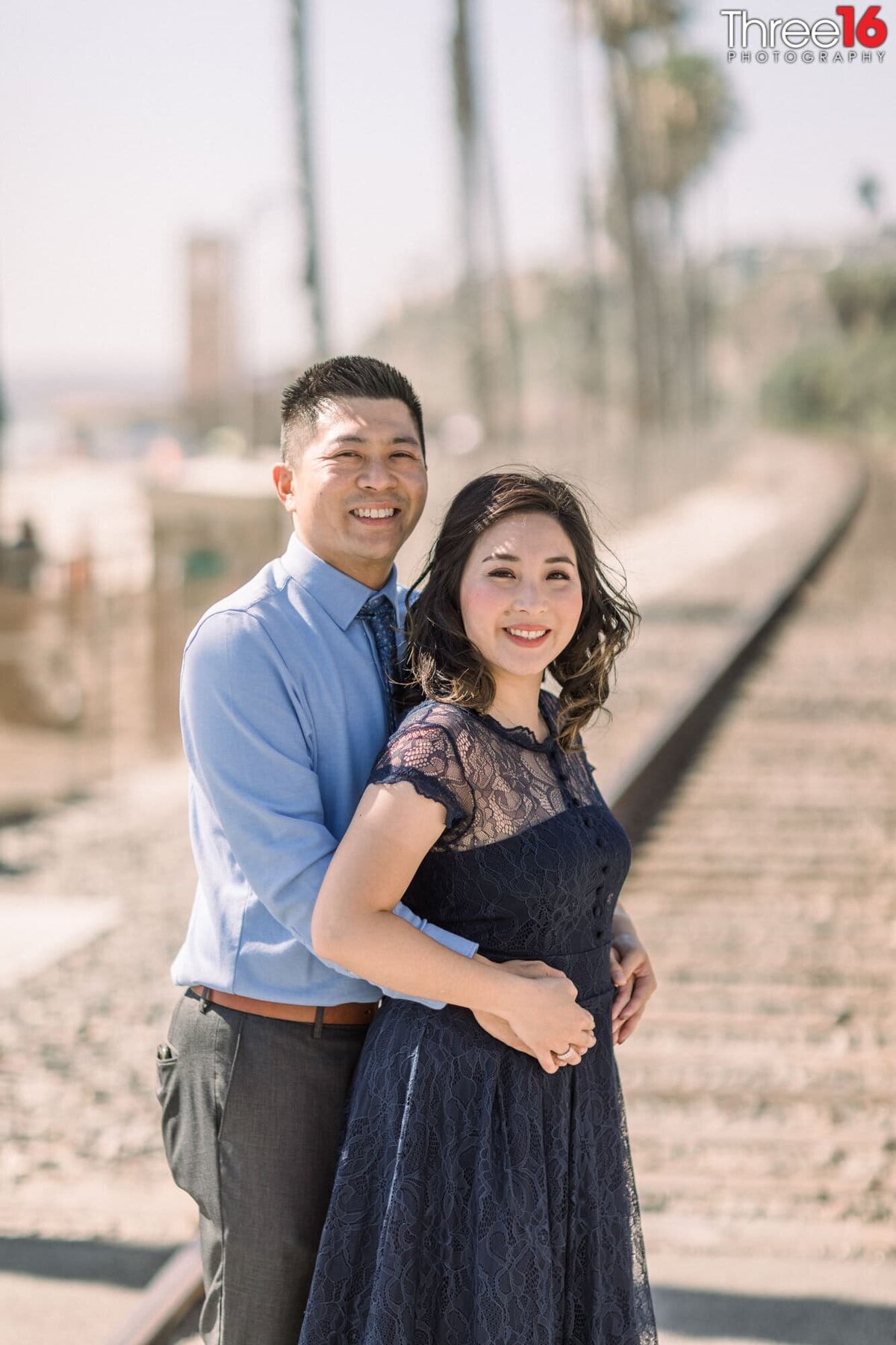 Groom to be embraces his Bride while standing on the train tracks behind the San Clemente Pier