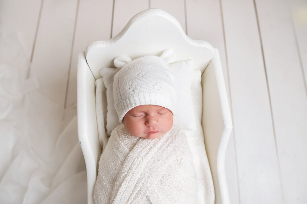 baby wrapped in white with white bear hat in white cradle