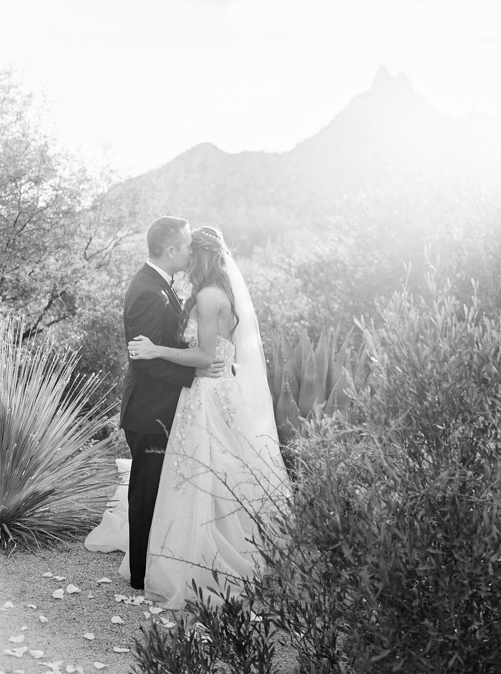 A timeless black and white wedding portrait of the bride and groom sharing a romantic kiss in a scenic outdoor setting. Classic love and wedding photography at its finest.