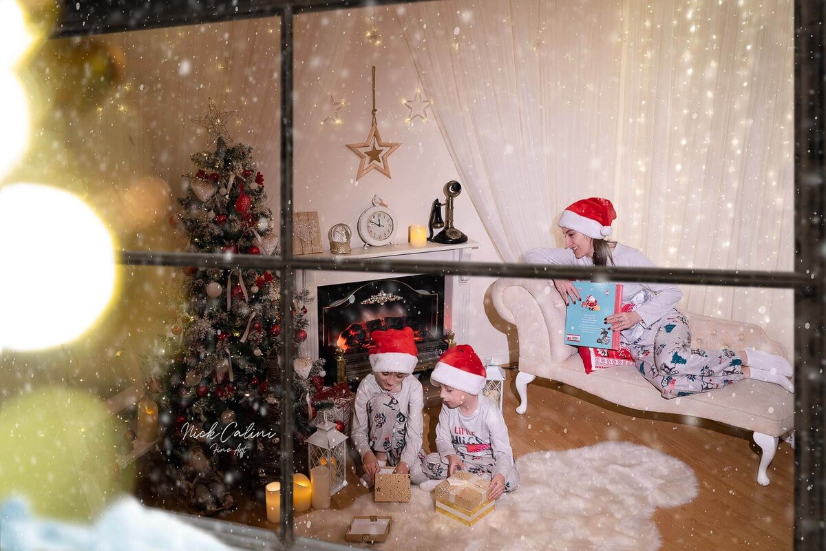 Children wearing Santa hats looking out window in Calini Weddings Studio - cozy Christmas setup with festive tree and warm fairy lights.