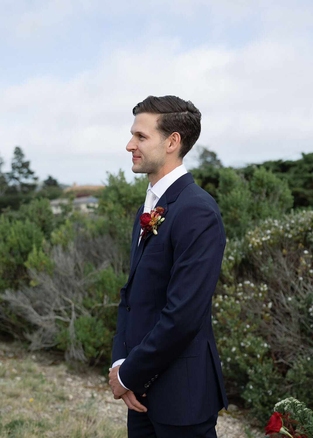 Groom in a navy suit standing with hands clasped before the ceremony