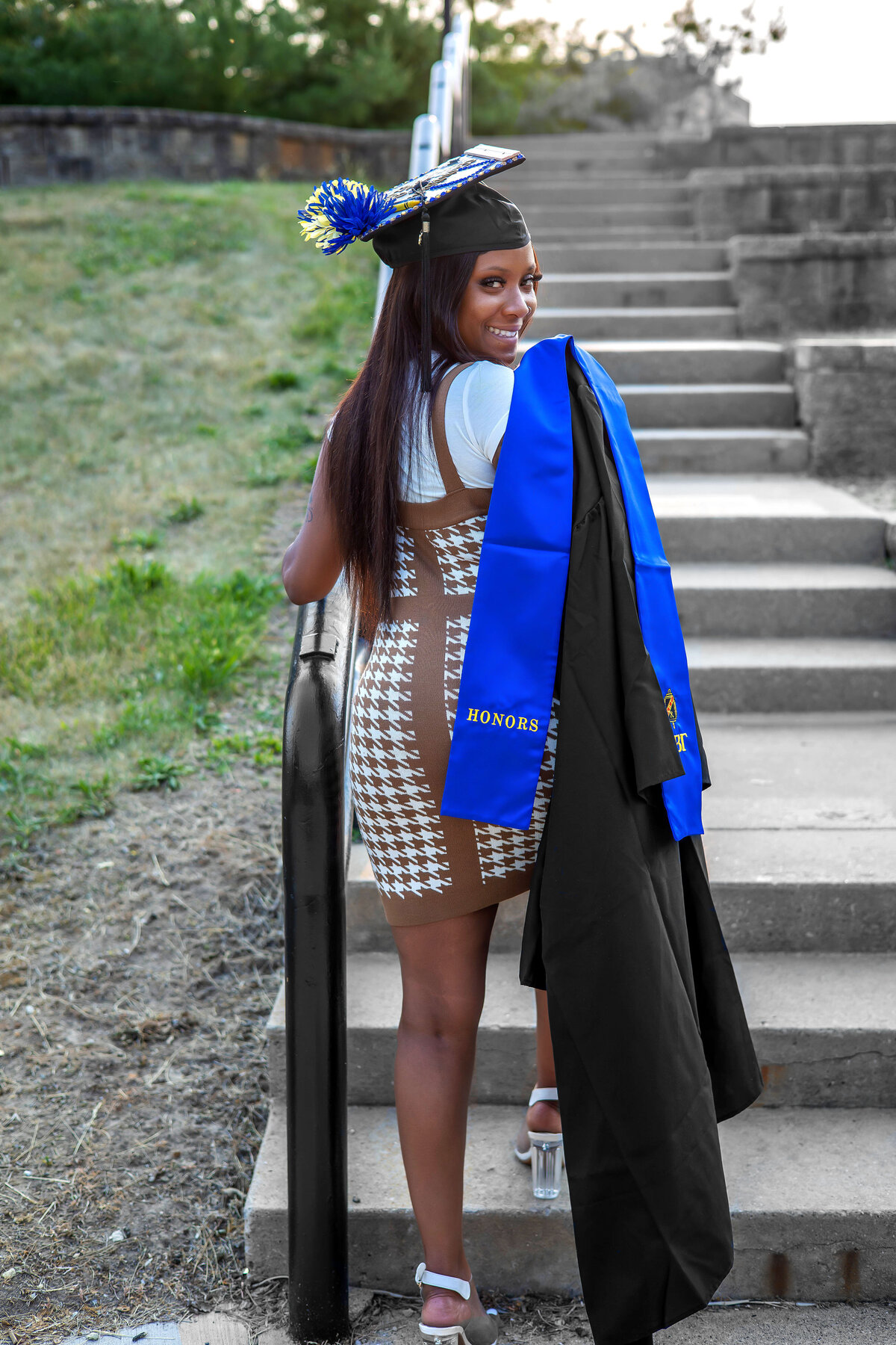 College graduate  holding graduation gown over her shoulder standing on a step
