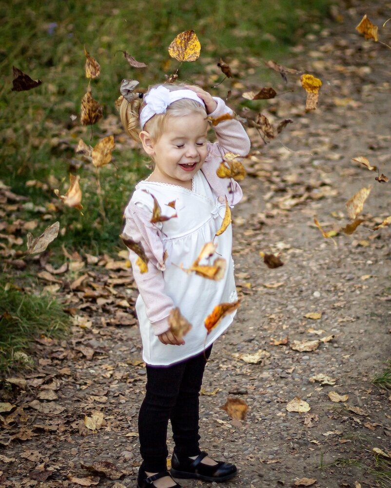 a little girl throwing autumn leaves in the air 
