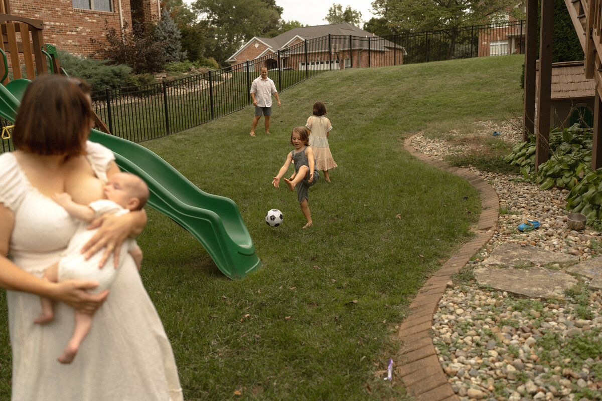 mom nursing baby in backyard while kids play