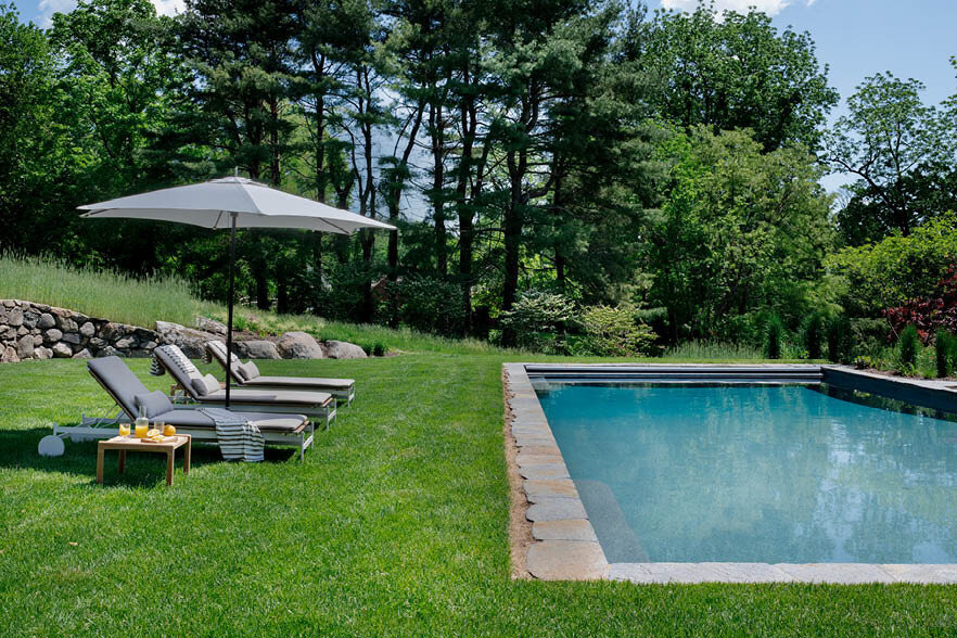 The pool at the historic Concord estate features modern chaise lounges from Design Within Reach and a Tucci umbrella, blending luxury and contemporary style.