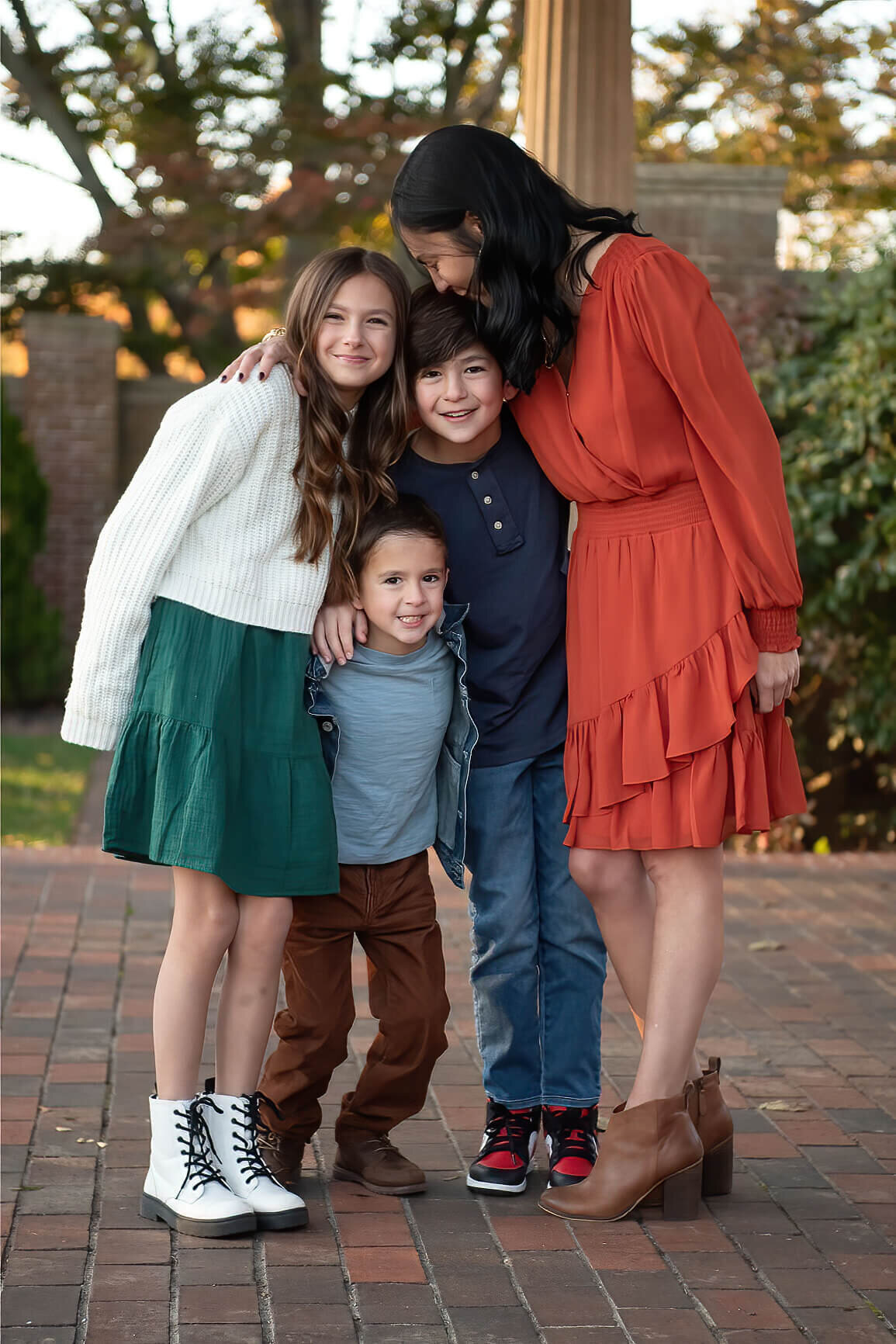 A mom looks down lovingly at her three children as they look at the camera in the garden of Lynch Park. 