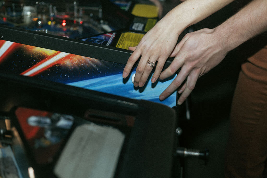 Two hands resting on a pinball machine together.