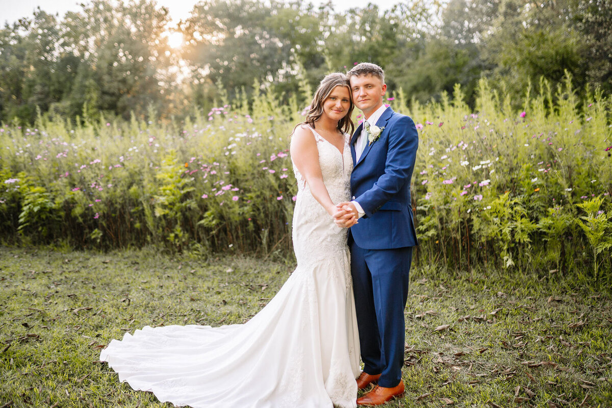 Bride and groom holding hands, posing in flower field at sunset