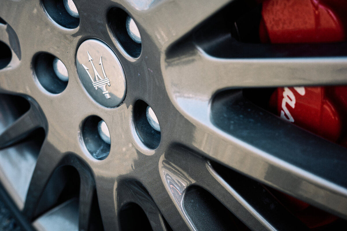 Detailed view of a Maserati alloy wheel featuring the signature trident emblem and red brake caliper, highlighting performance and luxury design.