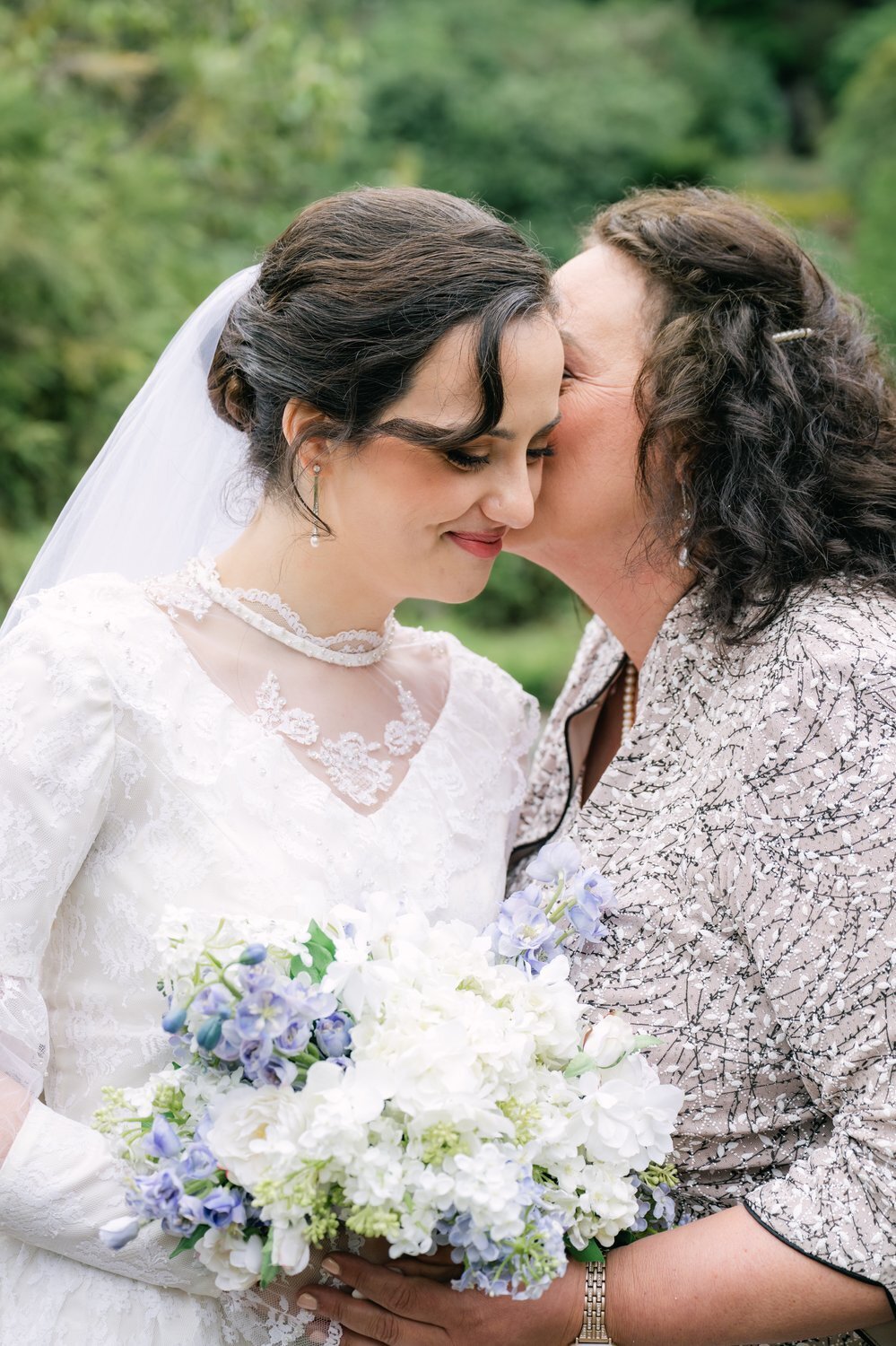 bride gets kiss from mother in garden before wedding