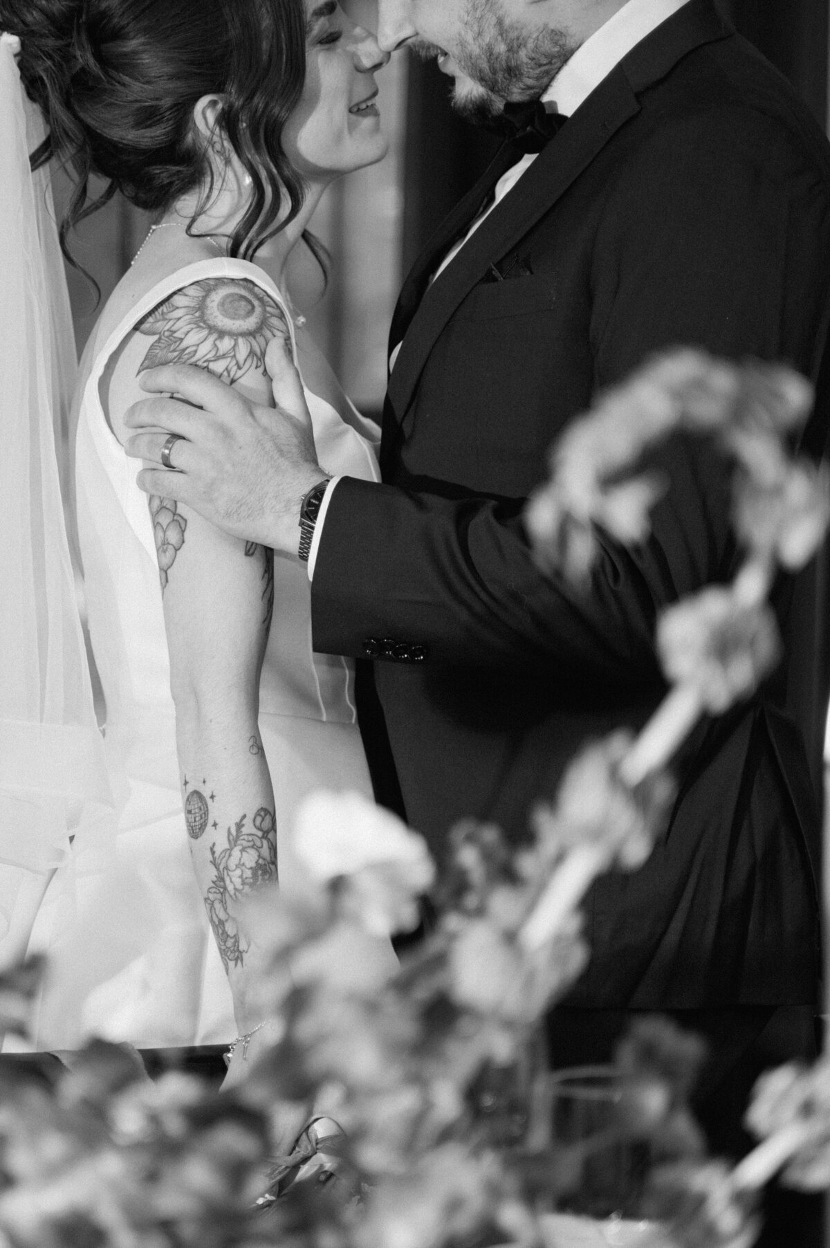 Emotional wedding moment captured with bride’s tattoo details and groom’s loving gesture.