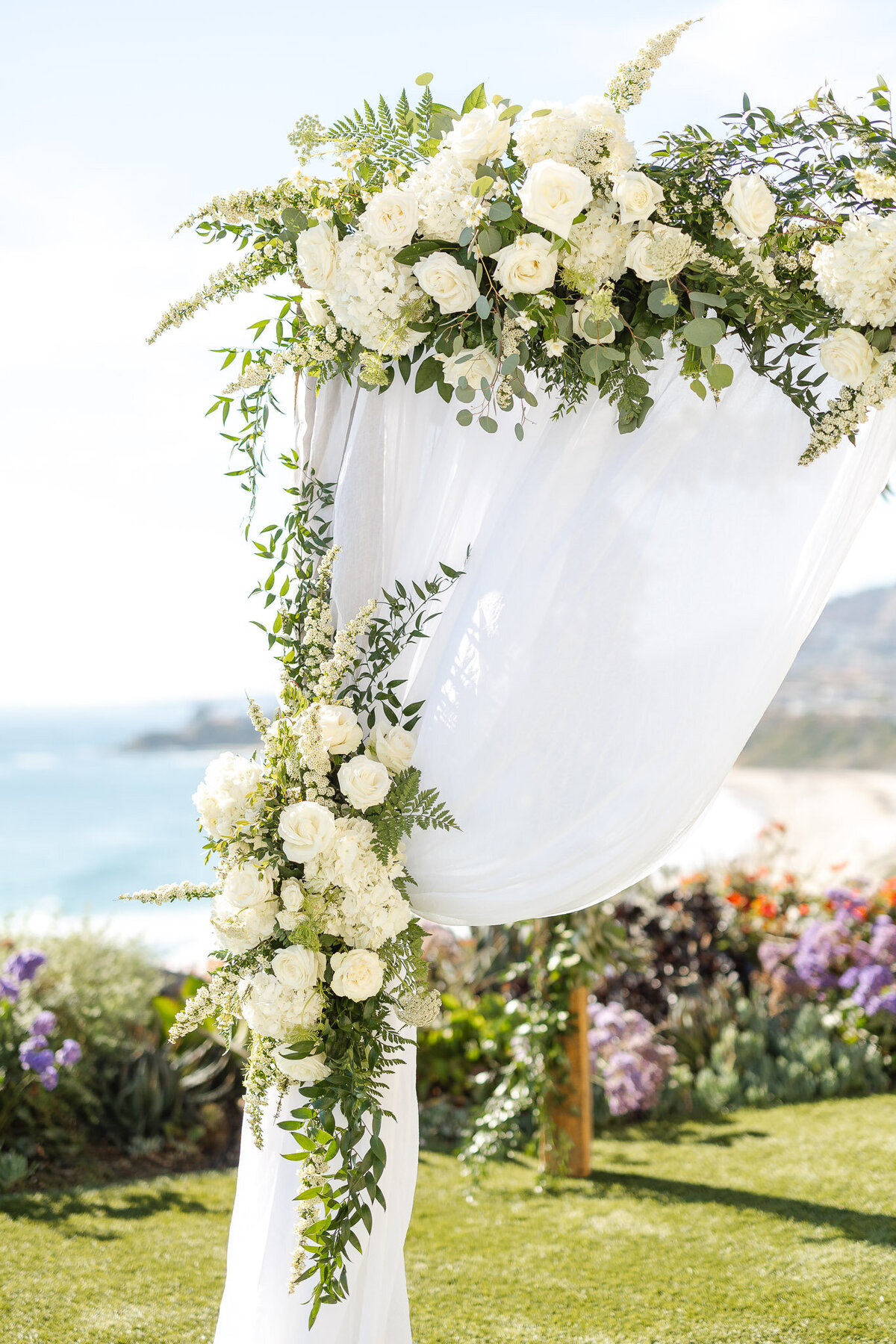 Elegant floral wedding arch with cascading white roses and greenery overlooking the ocean at Ritz Carlton Laguna Niguel