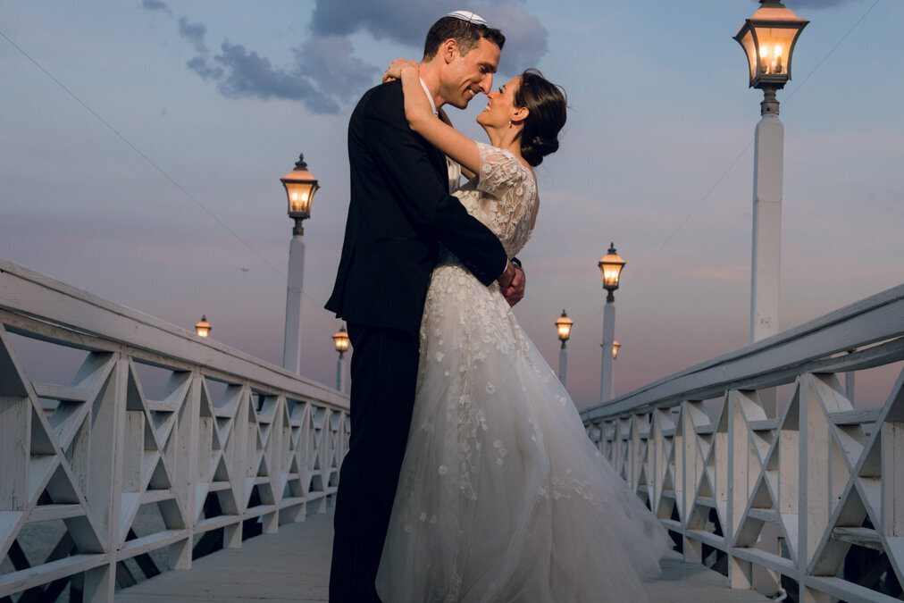 A man and woman hugging on a bridge at sunset.
