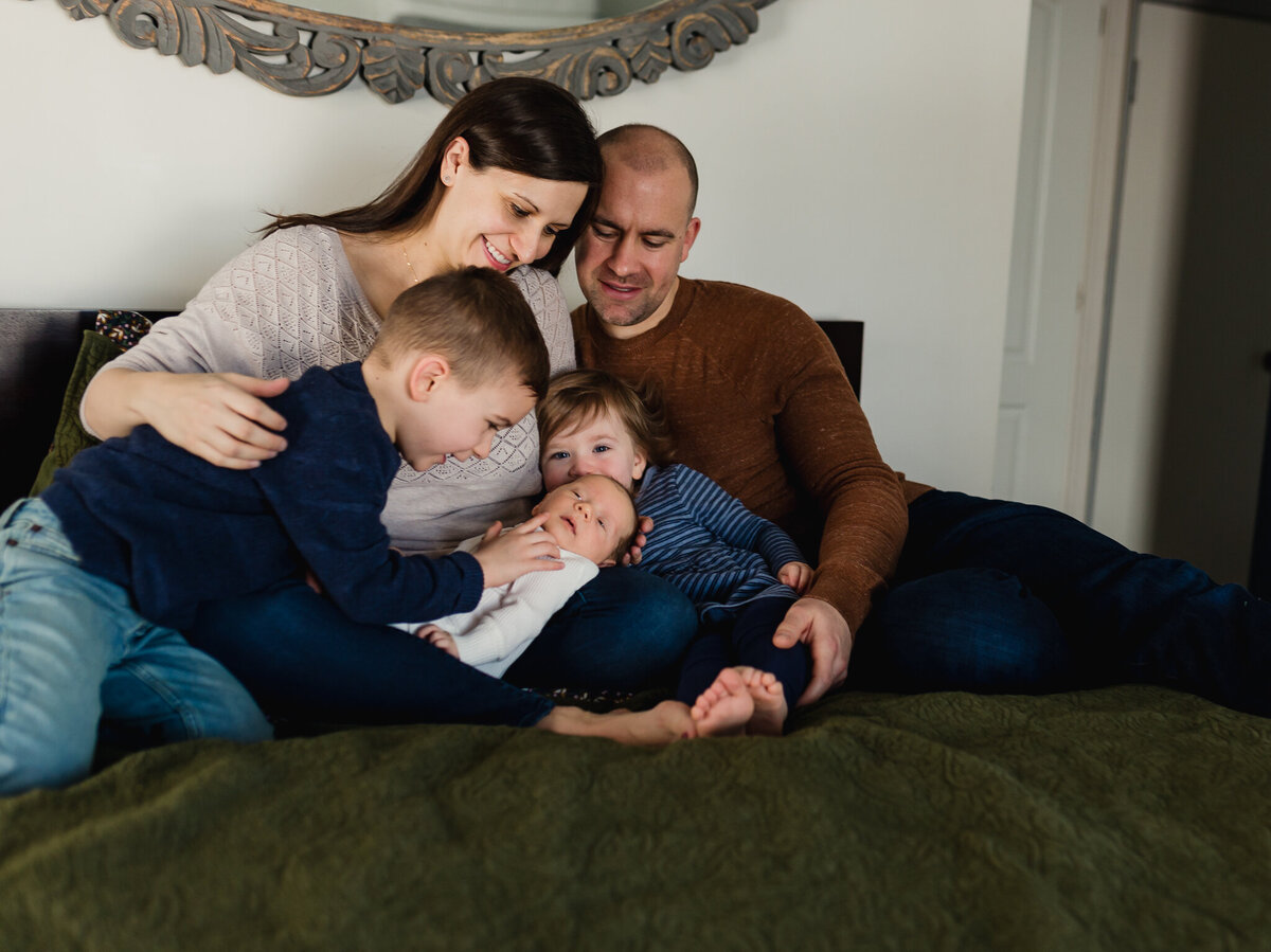 Family photo with mom, dad, children, and newborn baby sitting on bed.