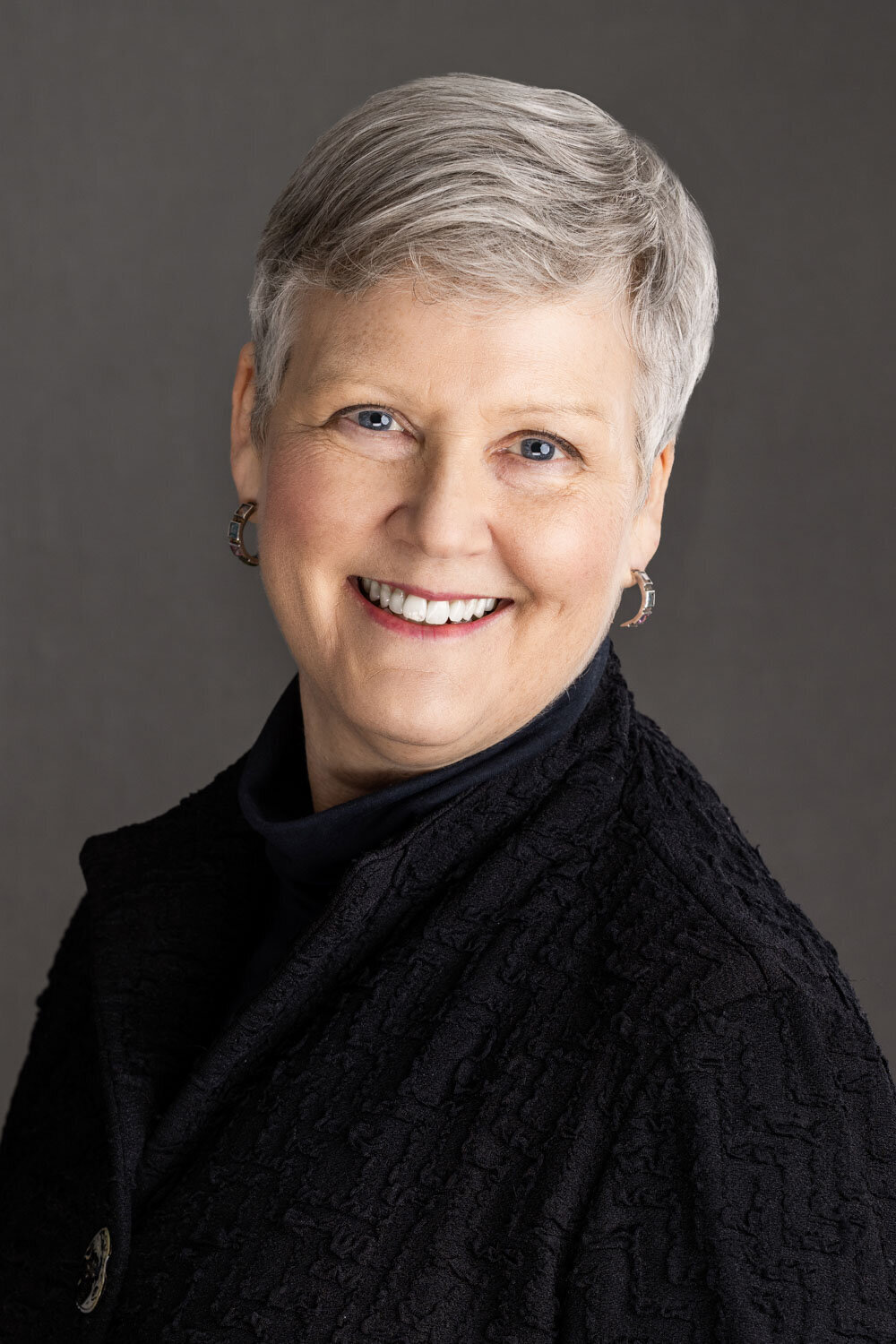Smiling woman with short gray hair in front of a dark backdrop