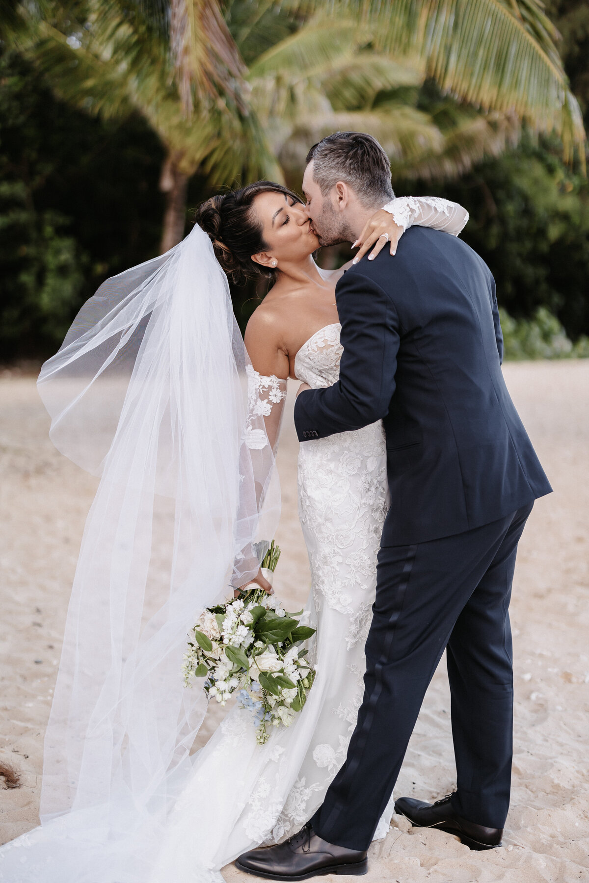 Bride and groom kissing on the beach dipped back, in front of palm trees