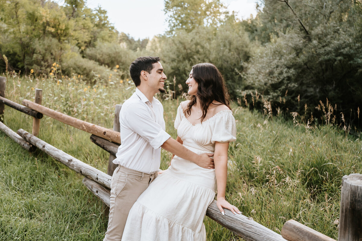 engaged couple sitting on wooden fence in the mountains
