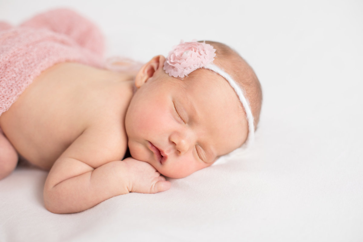 Newborn lying on tummy and wearing a pink flower headband