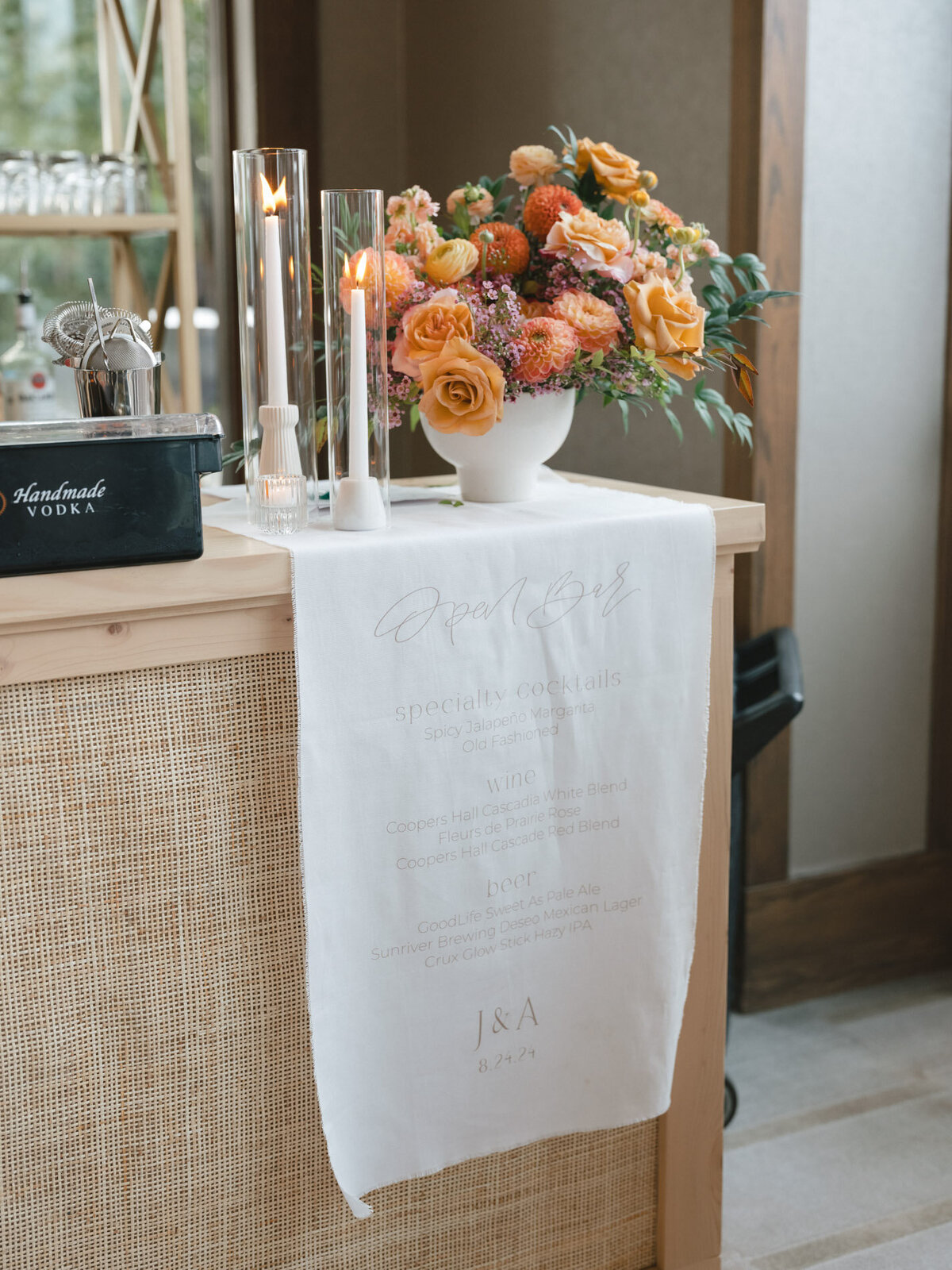 custom calligraphy bar menu on linen hanging from a rattan tabletop with florals representing full service design and calligraphy by Life in Letters.